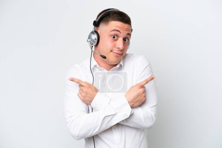 Photo for Telemarketer Brazilian man working with a headset isolated on white background pointing to the laterals having doubts - Royalty Free Image