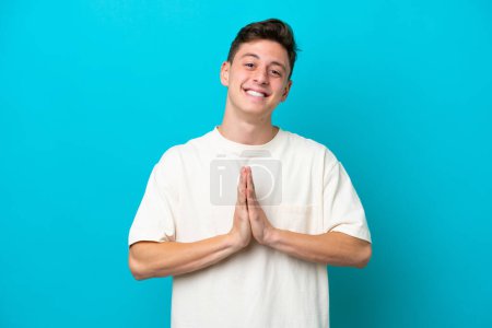 Photo for Young handsome Brazilian man isolated on blue background keeps palm together. Person asks for something - Royalty Free Image