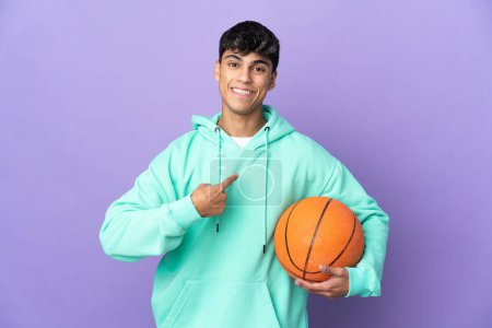 Téléchargez les photos : Jeune homme jouant au basket sur fond violet isolé avec expression faciale surprise - en image libre de droit
