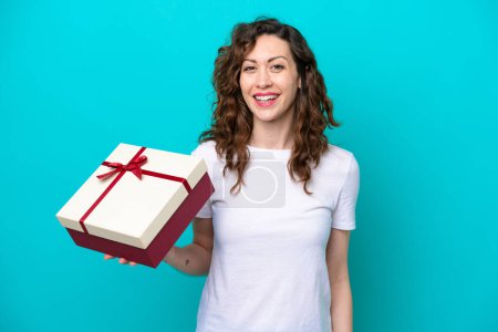 Photo for Young caucasian woman holding a gift isolated on blue background smiling a lot - Royalty Free Image