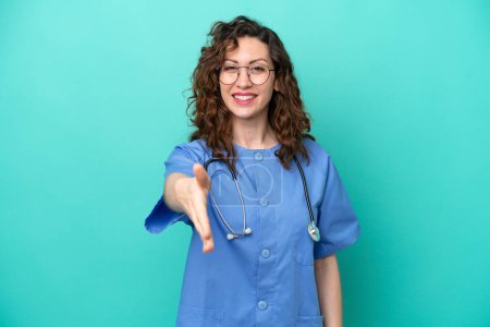 Téléchargez les photos : Jeune infirmière caucasienne femme isolée sur fond bleu serrant la main pour conclure une bonne affaire - en image libre de droit