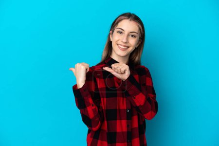 Téléchargez les photos : Jeune femme caucasienne isolée sur fond bleu pointant vers le côté pour présenter un produit - en image libre de droit