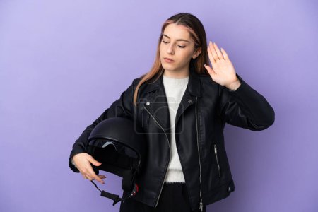 Téléchargez les photos : Jeune femme caucasienne tenant un casque de moto isolé sur fond violet faisant geste d'arrêt et déçu - en image libre de droit