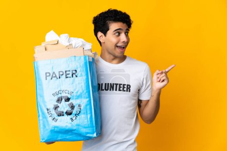 Téléchargez les photos : Jeune homme vénézuélien tenant un sac de recyclage rempli de papier à recycler dans l'intention de réaliser la solution tout en levant le doigt - en image libre de droit