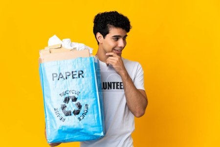 Téléchargez les photos : Jeune homme vénézuélien tenant un sac de recyclage plein de papier à recycler regardant vers le côté et souriant - en image libre de droit