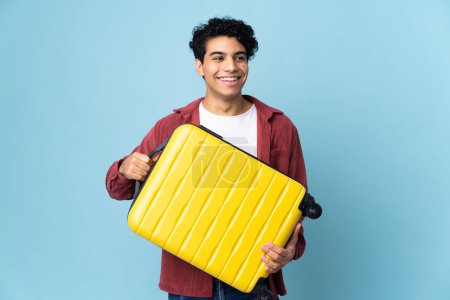 Photo for Young Venezuelan man isolated on blue background in vacation with travel suitcase - Royalty Free Image