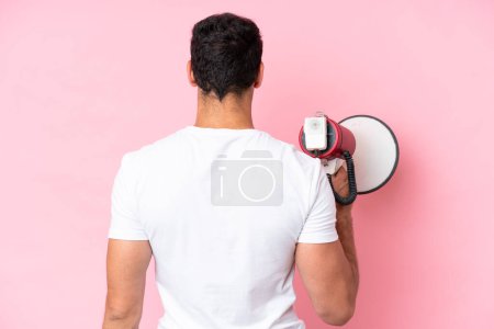 Téléchargez les photos : Jeune homme caucasien isolé sur fond rose tenant un mégaphone et en position arrière - en image libre de droit