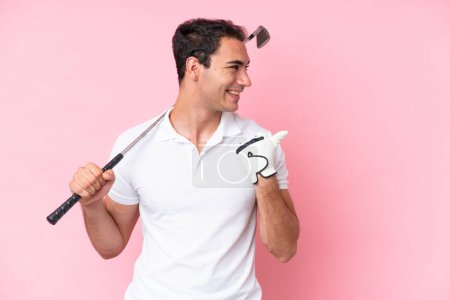 Foto de Joven jugador de golf hombre aislado sobre fondo rosa apuntando a un lado para presentar un producto - Imagen libre de derechos