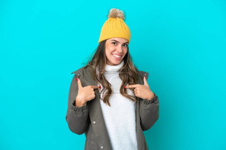 Téléchargez les photos : Jeune femme italienne vêtue d'une veste d'hiver et chapeau isolé sur fond bleu avec expression faciale surprise - en image libre de droit