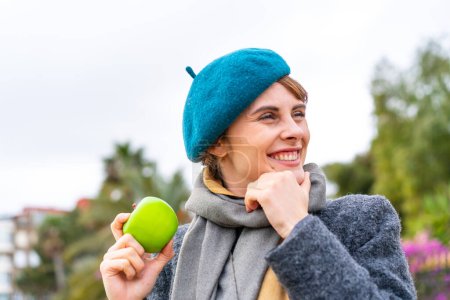 Foto de Mujer morena con una manzana al aire libre pensando en una idea y mirando al lado - Imagen libre de derechos