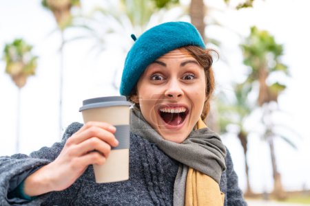 Téléchargez les photos : Femme brune tenant un café à emporter à l'extérieur avec une expression faciale surprise et choquée - en image libre de droit