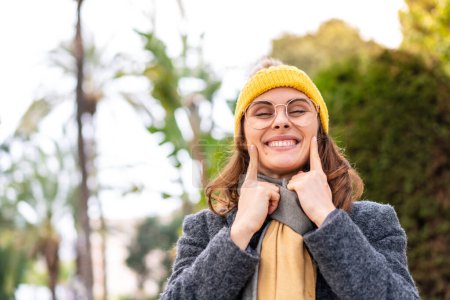 Téléchargez les photos : Brunette femme veste d'hiver en plein air souriant avec une expression heureuse et agréable - en image libre de droit