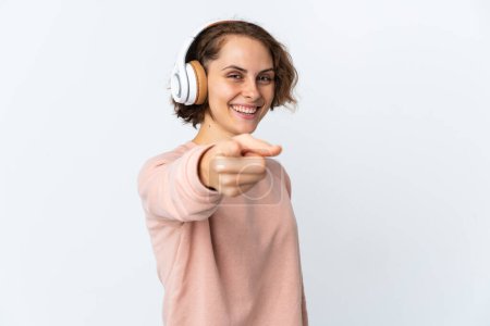 Téléchargez les photos : Jeune Anglaise isolée sur fond blanc écoutant de la musique et pointant vers l'avant - en image libre de droit