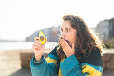 Photo for Young sport woman holding an avocado at outdoors with surprise and shocked facial expression - Royalty Free Image