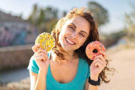 Photo for Young sport woman at outdoors holding donuts and surprised - Royalty Free Image