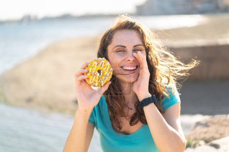 Téléchargez les photos : Jeune femme sportive tenant un beignet à l'extérieur criant avec la bouche grande ouverte - en image libre de droit