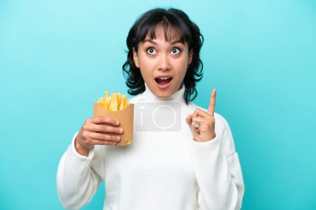 Photo for Young Argentinian woman holding fried chips isolated on blue background thinking an idea pointing the finger up - Royalty Free Image