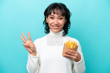 Photo for Young Argentinian woman holding fried chips isolated on blue background happy and counting three with fingers - Royalty Free Image