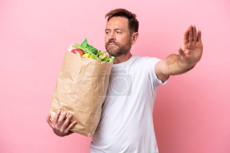 Photo for Middle age man holding a grocery shopping bag isolated on pink background making stop gesture and disappointed - Royalty Free Image