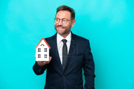 Foto de Inmobiliaria agente de mediana edad hombre aislado en fondo azul pensando una idea mientras mira hacia arriba - Imagen libre de derechos