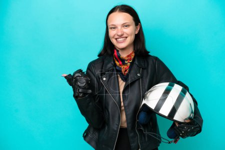 Téléchargez les photos : Jeune femme caucasienne avec un casque de moto isolé sur fond bleu pointant vers le côté pour présenter un produit - en image libre de droit