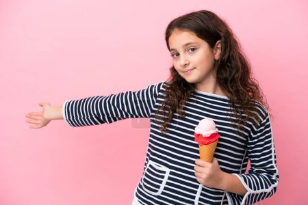 Téléchargez les photos : Petite fille caucasienne tenant une crème glacée isolée sur fond rose étendant les mains sur le côté pour inviter à venir - en image libre de droit