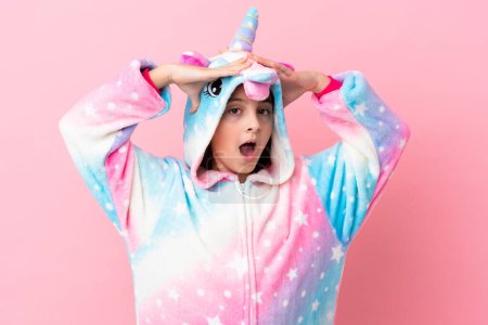 Foto de Pequeña mujer caucásica con un pijama unicornio aislado sobre fondo rosa con expresión sorpresa - Imagen libre de derechos