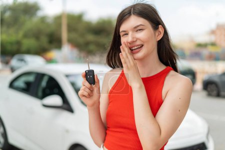 Téléchargez les photos : Jeune jolie Ukrainienne tenant des clés de voiture à l'extérieur chuchotant quelque chose - en image libre de droit