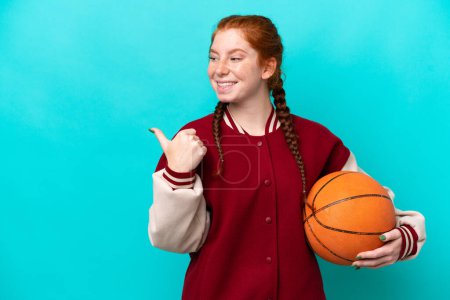 Téléchargez les photos : Jeune femme rougeâtre jouant au basket isolé sur fond bleu pointant vers le côté pour présenter un produit - en image libre de droit
