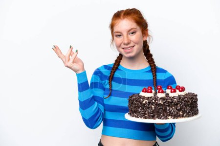 Foto de Young reddish woman holding birthday cake isolated on white background extending hands to the side for inviting to come - Imagen libre de derechos