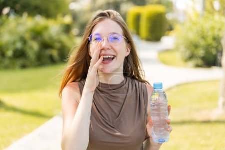 Téléchargez les photos : Française avec des lunettes tenant une bouteille d'eau à l'extérieur criant avec la bouche grande ouverte - en image libre de droit