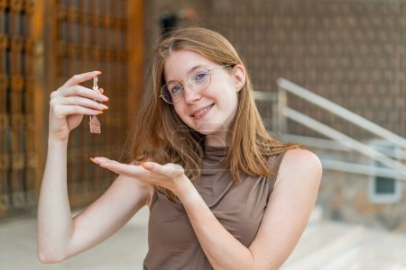 Foto de Joven chica francesa con gafas al aire libre sosteniendo las llaves del hogar con expresión feliz - Imagen libre de derechos