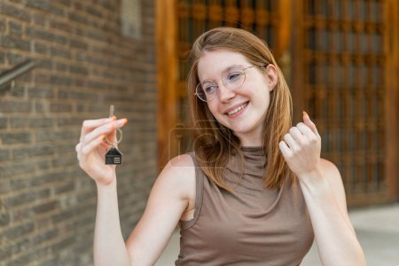 Téléchargez les photos : Française avec des lunettes tenant les clés de la maison à l'extérieur célébrant une victoire - en image libre de droit