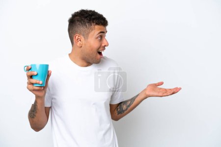 Foto de Joven brasileño sosteniendo taza de café aislado sobre fondo blanco con expresión facial sorpresa - Imagen libre de derechos