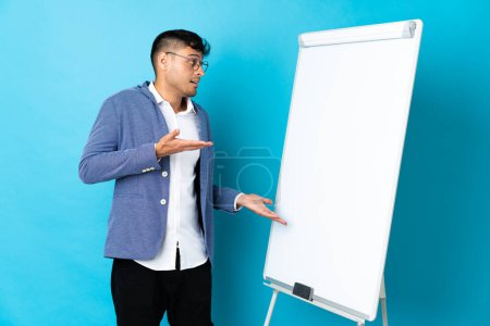 Photo for Young Colombian man isolated on blue background giving a presentation on white board and with surprise expression - Royalty Free Image
