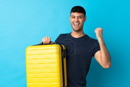 Téléchargez les photos : Jeune Colombien isolé sur fond bleu en vacances avec valise de voyage - en image libre de droit
