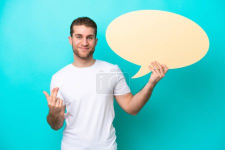Photo for Young caucasian man isolated on blue background holding an empty speech bubble and doing coming gesture - Royalty Free Image