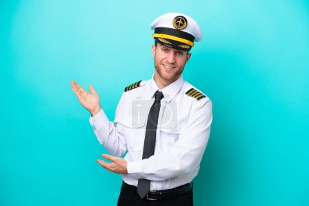 Airplane caucasian pilot isolated on blue background extending hands to the side for inviting to come