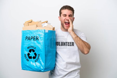 Young caucasian man holding a recycling bag full of paper to recycle isolated on white background shouting with mouth wide open