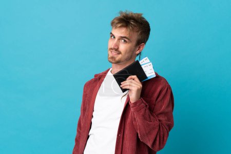 Téléchargez les photos : Jeune homme blond beau isolé sur fond bleu heureux en vacances avec passeport et billets d'avion - en image libre de droit