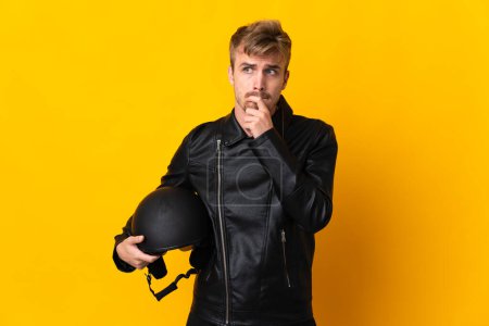 Téléchargez les photos : Homme avec un casque de moto isolé sur fond jaune ayant des doutes et la pensée - en image libre de droit