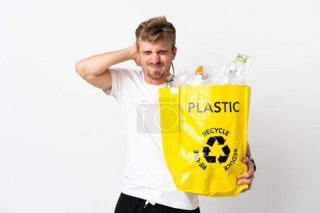 Foto de Joven hombre rubio sosteniendo una bolsa de reciclaje llena de papel para reciclar aislado sobre fondo blanco frustrado y cubriendo las orejas - Imagen libre de derechos