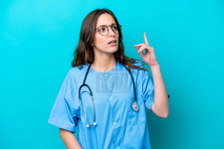 Téléchargez les photos : Young surgeon doctor woman isolated on blue background thinking an idea pointing the finger up - en image libre de droit
