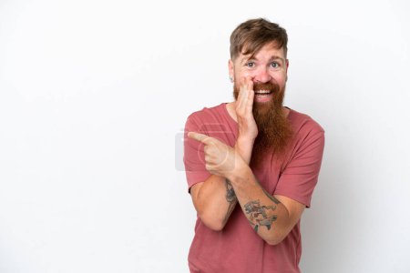 Photo for Redhead man with long beard isolated on white background pointing to the side to present a product and whispering something - Royalty Free Image