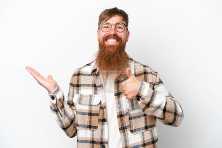 Photo for Redhead man with long beard isolated on white background holding copyspace imaginary on the palm to insert an ad and with thumbs up - Royalty Free Image