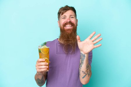 Photo for Redhead man with long beard holding a cocktail isolated on blue background saluting with hand with happy expression - Royalty Free Image
