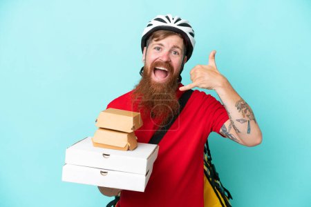 Photo for Delivery man holding pizzas and burgers isolated on blue background making phone gesture. Call me back sign - Royalty Free Image