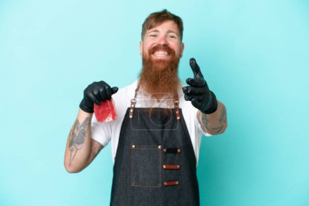 Photo for Butcher man wearing an apron and serving fresh cut meat isolated on blue background shaking hands for closing a good deal - Royalty Free Image