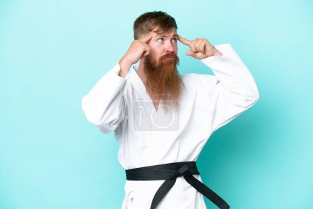 Foto de Pelirroja con barba larga haciendo karate aislado sobre fondo azul teniendo dudas y pensando - Imagen libre de derechos
