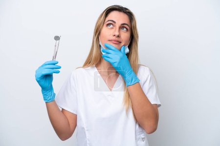 Téléchargez les photos : Dentiste femme tenant des outils isolés sur fond blanc ayant des doutes - en image libre de droit